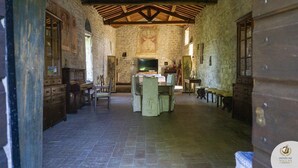 Una habitación rústica con paredes de piedra, techo de madera, una mesa central y bancos.