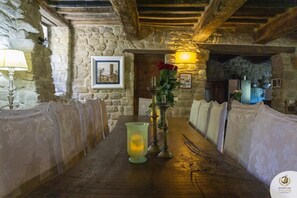 Een rustieke kamer met stenen muren, een houten tafel, twee kaarsen en een vaas met rode bloemen.