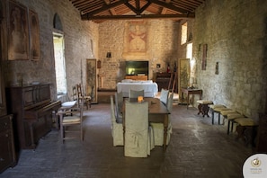 Quarto rústico com paredes de pedra, teto de madeira, cama, televisão e área de refeições com cadeiras e mesa.