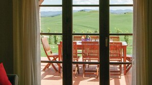 Quarto com vista para um campo verde pela janela. Há uma mesa com cadeiras e uma tigela de frutas sobre ela.