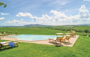 Una piscina con sillones de descanso y una mesa, rodeada de césped y una vista panorámica de colinas ondulantes y montañas.
