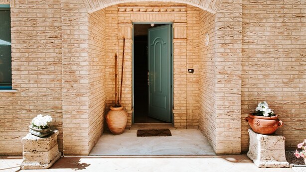 A brick building entrance with a green door, a large vase, and potted plants. - Villa Collina Sul Mare (Porto San Giorgio)