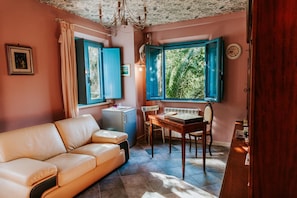 A cozy room with a sofa, a small table, a chair, a desk, and a window with blue shutters.
