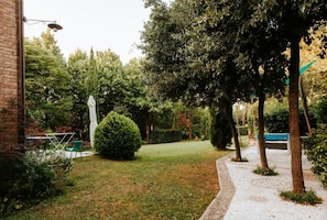A well-maintained garden with a paved path, neatly trimmed hedges, and a variety of trees.