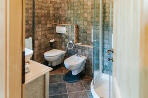 A bathroom with a toilet, bidet, sink, and a glass-enclosed shower area.
