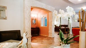 A hotel lobby with a marble floor, a reception desk, a red armchair, and white orchids in a vase. - Villa Collina Sul Mare (Porto San Giorgio)