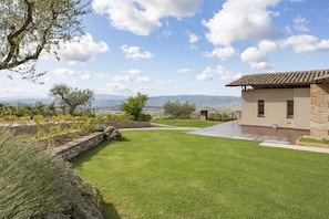 Ein modernes Haus mit Terrasse, einem gepflegten Rasen und Blick auf ferne Hügel.