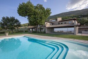 Eine moderne Villa mit Swimmingpool, überdachter Terrasse und Blick auf die umliegenden Hügel.