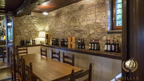 A rustic interior with a stone wall, wooden table, and chairs, and a wine rack with bottles. - Villa Antico Incanto (Monte Castello di Vibio)