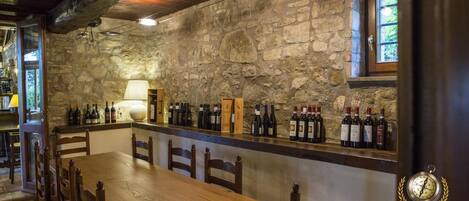 Un interior rústico con pared de piedra, mesa y sillas de madera, y una estantería para vinos con botellas.