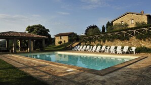 Une piscine avec des chaises longues, un bâtiment en pierre et une pergola.