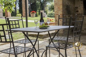 An outdoor patio with a table set for two, featuring a bottle of wine, a glass, and a plate of greens. - Villa Cattaneo (Gualdo Cattaneo)