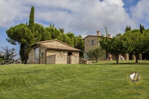 Una villa de piedra con techo de tejas, rodeada por un césped cuidado y árboles.