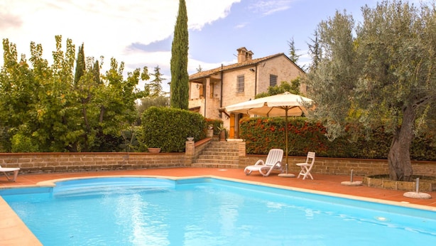 A swimming pool with lounge chairs and a patio area, surrounded by trees and a building with a tiled roof. - Villa Anna (Giulianova)