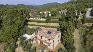Ein Steinhaus mit Ziegeldach und kleinem Balkon, umgeben von üppigem Grün und einem Fluss.