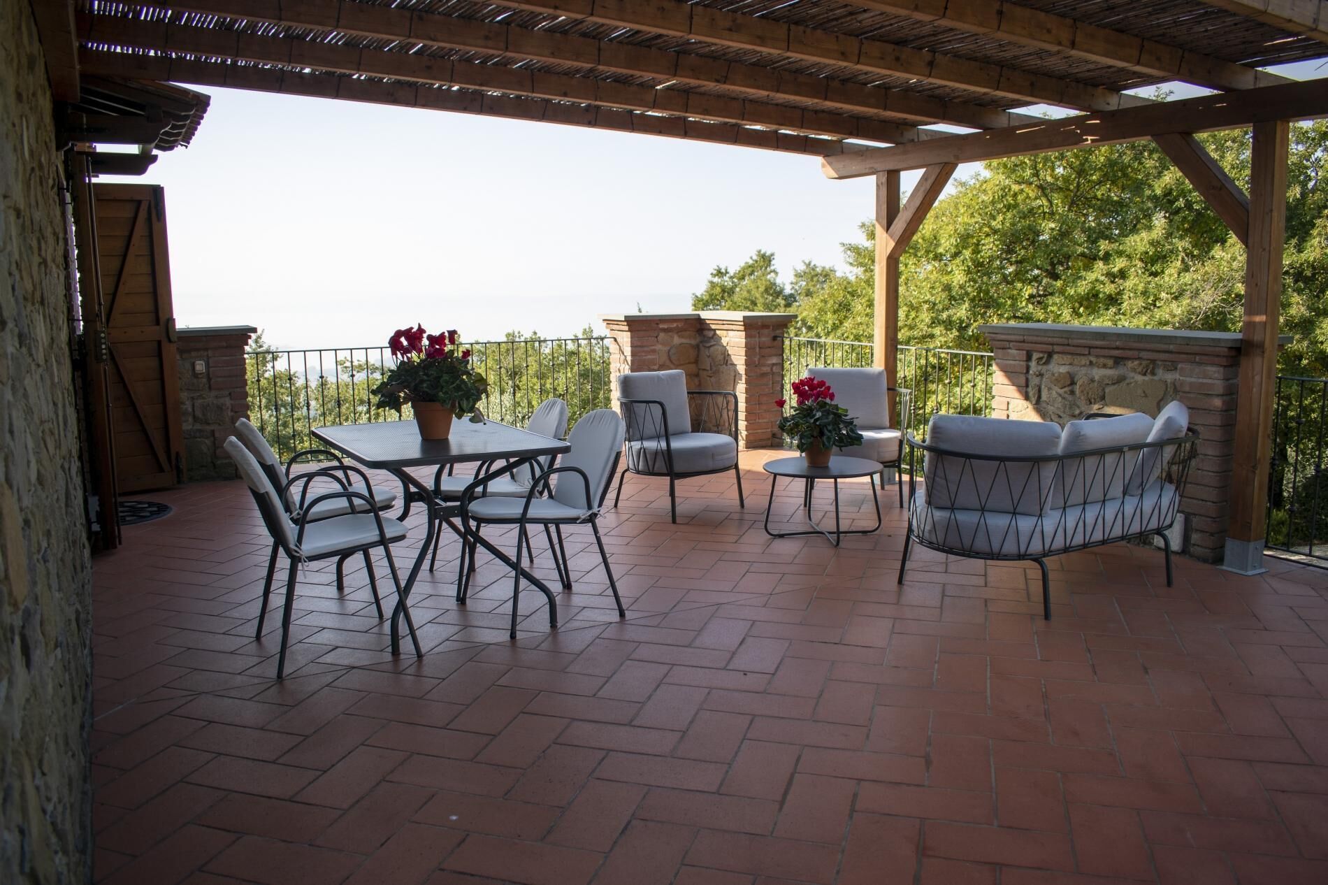 Un patio exterior con pérgola, muros de piedra y arreglos de asientos que incluyen una mesa y sillas.