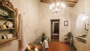 Un pasillo estrecho con una bañera, un candelabro, un espejo y una silla.