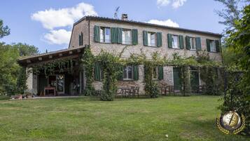 A two-story stone building with green shutters, a covered porch, and outdoor seating.
