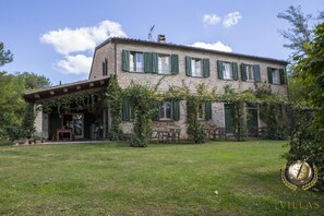 A two-story stone building with green shutters, a covered porch, and outdoor seating.