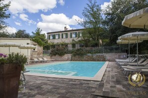 A swimming pool with lounge chairs and umbrellas, surrounded by stone walls and greenery.