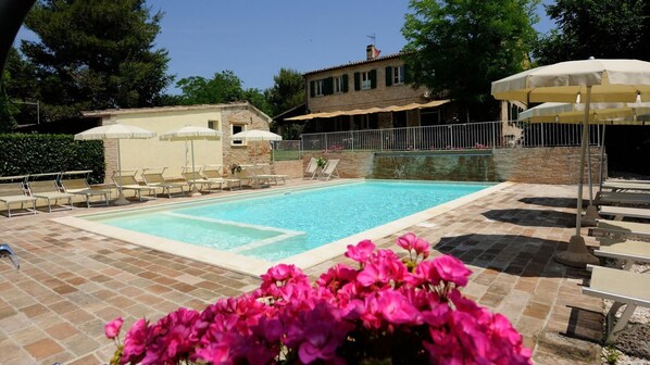 A rectangular swimming pool with a tiled deck, surrounded by lounge chairs and umbrellas.