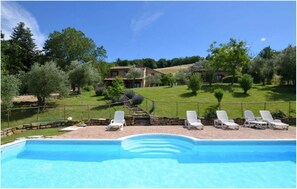 Una piscina con sillas de descanso, un sendero de piedra y una casa con jardín al fondo.