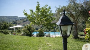 A pool area with a view of hills, a lamp post, and a white umbrella. - Villa Claudia (Gualdo)
