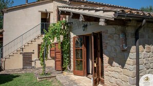 A stone building with a tiled roof, a wooden staircase, and a small garden area. - Villa Claudia (Gualdo)