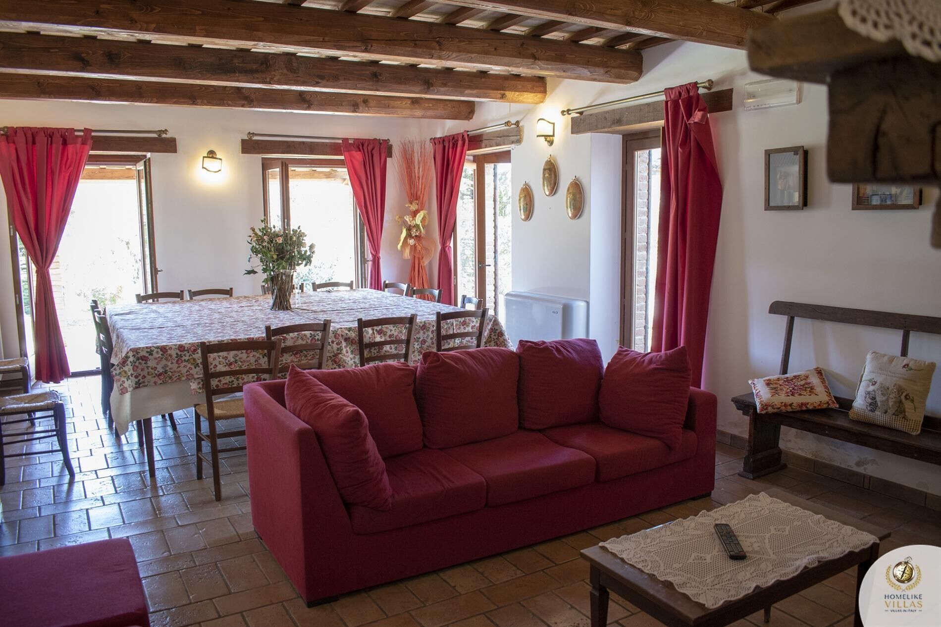 Un salon chaleureux avec un canapé rouge, une table à manger avec des chaises et un coin cuisine équipé d’un réfrigérateur.