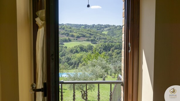 A view from a room with a balcony overlooking a green landscape and a body of water. - Villa Claudia (Gualdo)