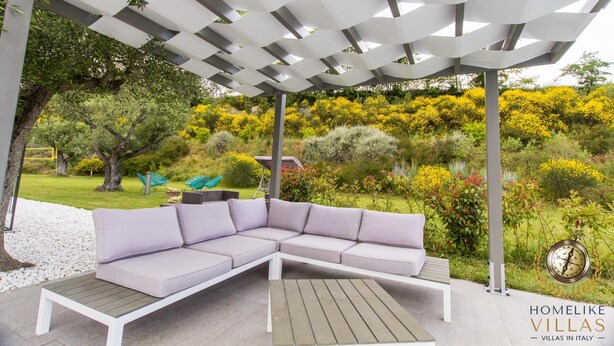 A modern outdoor seating area with a white pergola, a sectional sofa, and a wooden table. - Villa Giorgi (Cingoli)
