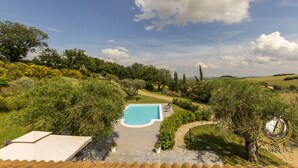 A swimming pool with a paved deck, surrounded by lush greenery and trees. - Villa Giorgi (Cingoli)