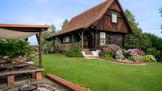 Une maison rustique en bois, dotée d’un toit en pente, d’un porche à l’avant et d’un chemin en briques menant à l’entrée.
