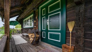 Une véranda en bois avec une porte verte, un banc en bois et un balai appuyé contre le mur.