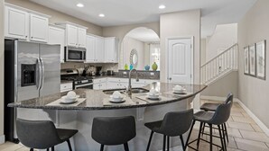 Una cocina moderna con armarios blancos, un refrigerador de acero inoxidable, un microondas y una isla con encimera de granito y taburetes de bar.