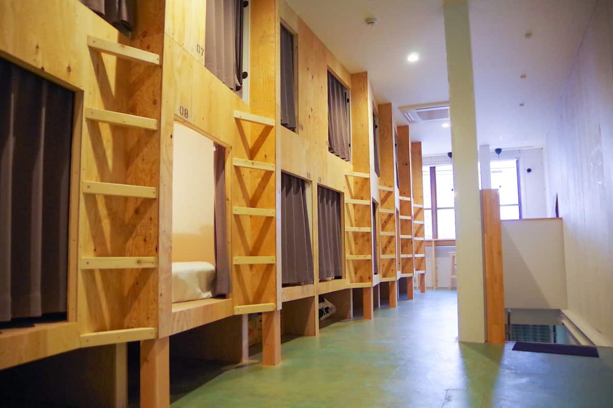 A row of wooden bunk beds with ladders, a green floor, and a hallway leading to a door.