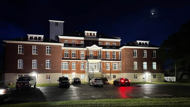 A multi-story building with a central entrance, parking lot, and a moon in the sky. - The Couvent (Sainte-Anne-des-Monts)