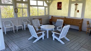 A covered outdoor seating area with white chairs and a table, wooden benches, and large windows. - The Couvent (Sainte-Anne-des-Monts)