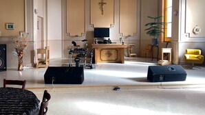 A spacious room with a piano, a drum set, a television, and a yellow chair. - The Couvent (Sainte-Anne-des-Monts)