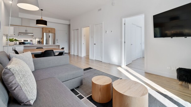 Een moderne woonkamer met een grijze modulaire bank, een houten salontafel en een eetgedeelte, met een keuken op de achtergrond.