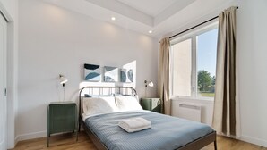 Een moderne slaapkamer met een bed, nachtkastjes, kunstwerken en een groot raam met gordijnen.