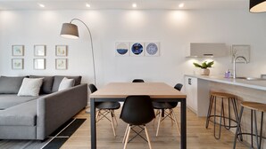 Een moderne woonkamer met een grijze bank, een houten eettafel, zwarte stoelen en een keuken met een spoelbak en barstoelen.