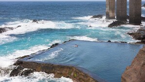 A coastal pool with waves crashing against rocks, a clear sky, and three large stone structures in the background. - Home2Book Stunning View La Era2 de Hermigua & Wifi (Hermigua)