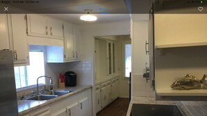 A kitchen with white cabinets, a granite countertop, a stainless steel sink, and a black stove.