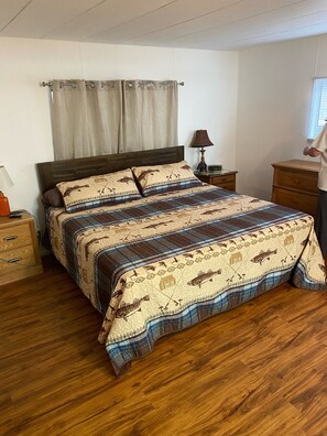 Een slaapkamer met een houten bed, een nachtkastje met een lamp, een dressoir en een raam met jaloezieën.