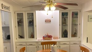 A dining room with a wooden table and chairs, a ceiling fan, and a cabinet with glass doors displaying various items.