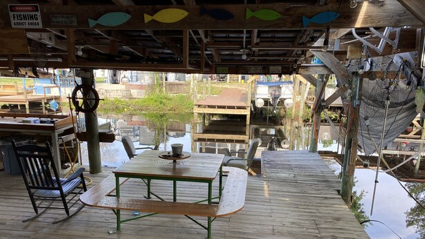 An outdoor wooden deck with picnic tables and chairs, surrounded by fishing equipment and signs.