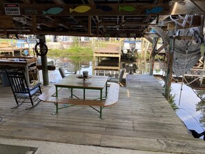Een houten terras buiten, met picknicktafels en stoelen, omringd door visgerei en borden.