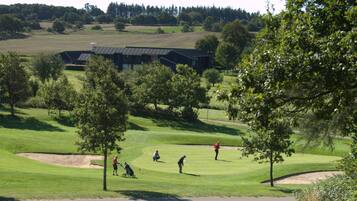 En golfbane med sandbunkere, træer og en bygning i baggrunden.