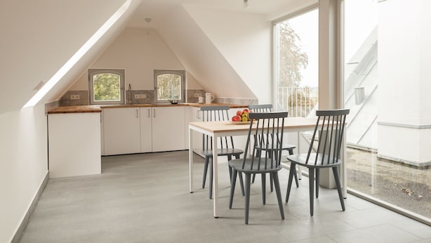 A modern kitchen with white cabinets, a wooden countertop, and a dining area with grey chairs. - Gutshaus Üselitz (Poseritz)